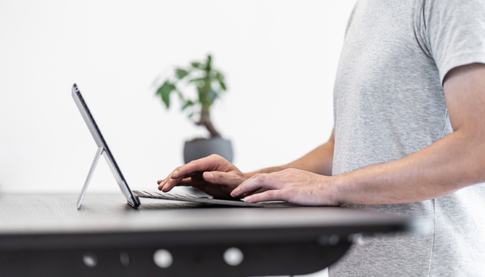 A closeup of a man at a standing desk on his laptop.