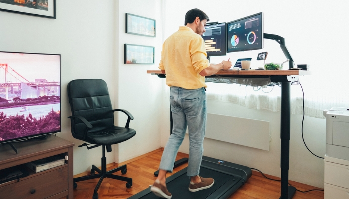 A man using a walking pad while working at his standing desk at home.