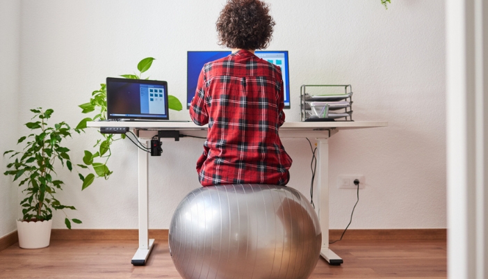 A woman sits on a silver yoga ball while working from home. 