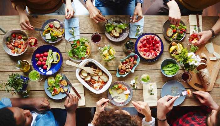 An overhead shot of hands reaching for food on a long, wooden dining table.