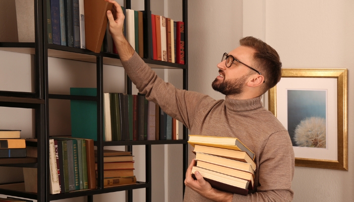 A man pulling books off of his bookcase to read