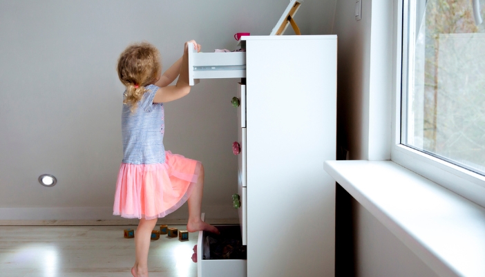 A child using drawers to climb up a drawer chest