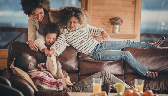Family being playful around dad laying down on the leather couch