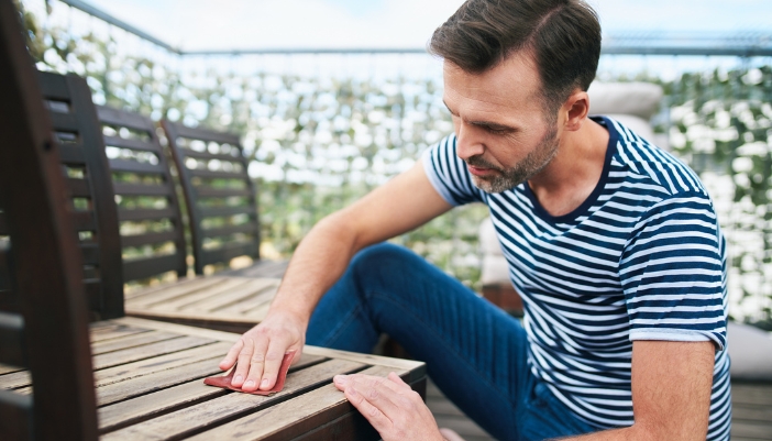 Man prepping wooden garden chairs for a fresh coat of sealant