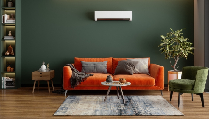 A rust orange colored couch sits in front of a deep green wall in a modern living room