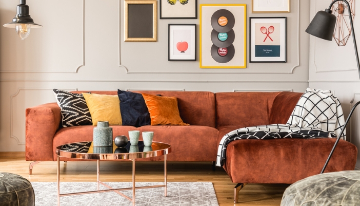 A rust colored L-shaped couch sits in a room of retro accents and fall colors.
