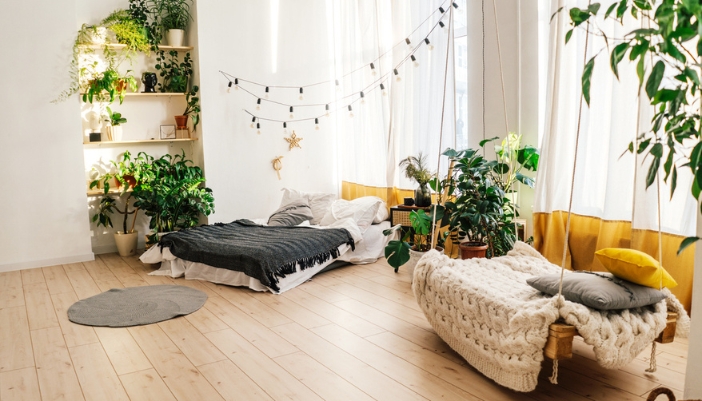 A brightly lit bedroom with light wood floors, natural materials, and many plants.