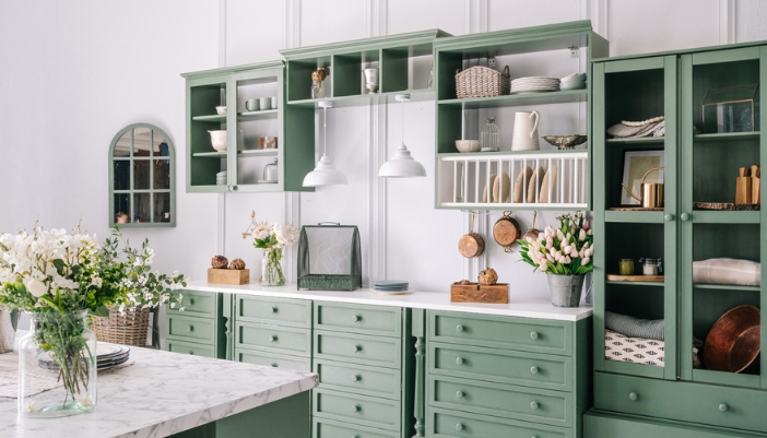 A kitchen with green cabinetry, neutral colored accents, and several flower vases.