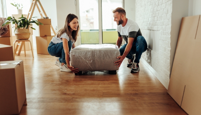 A man and a woman work together to lift a square footrest in a packed-up home.