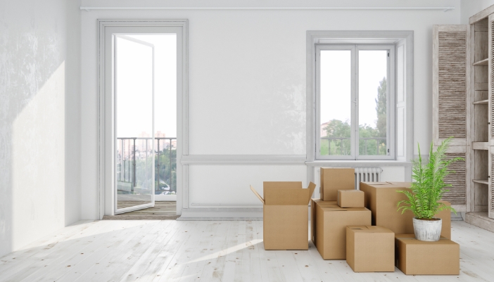 An empty room with white walls and white wooden floors and many cardboard boxes piled up in the middle.