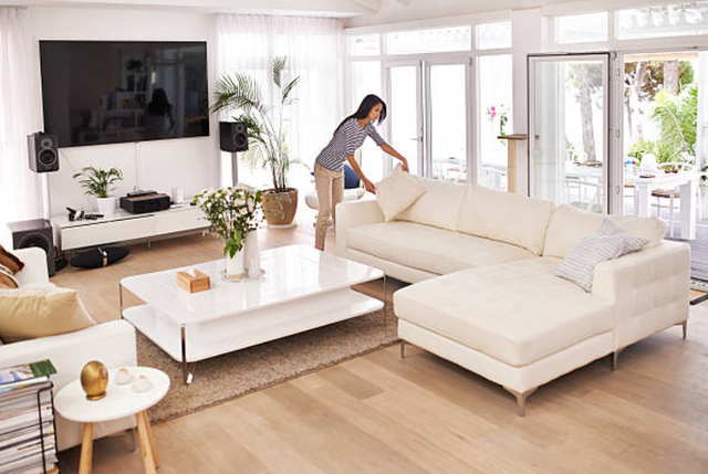 front view of a large living room with white furniture and a woman fluffing a throw pillow on the couch