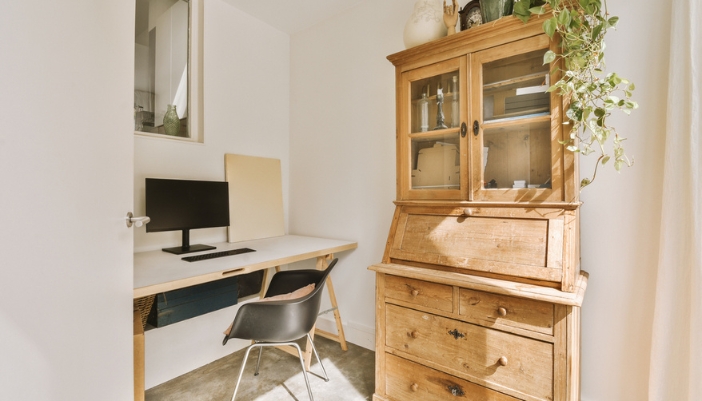 A home office with a laptop on a desk and a natural wooden hutch beside it.
