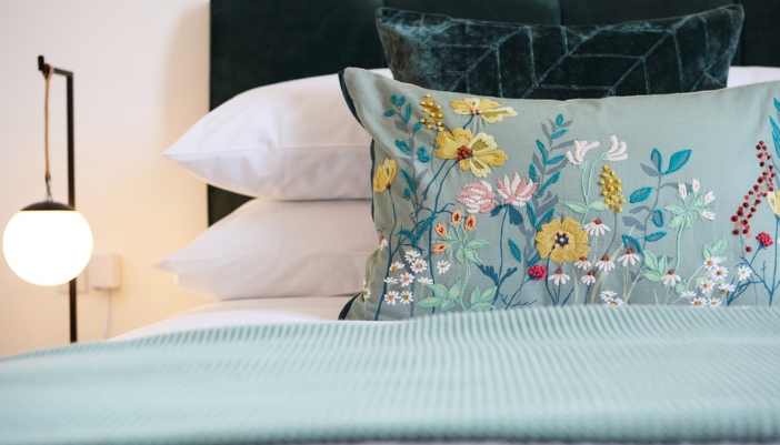 A green and white bedspread with pillows and one floral embroidered pillow. 