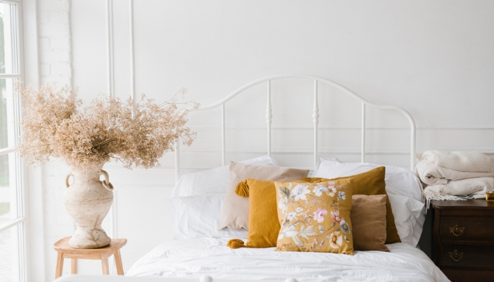 A white bedspread with golden throw pillows and one floral throw pillow. 