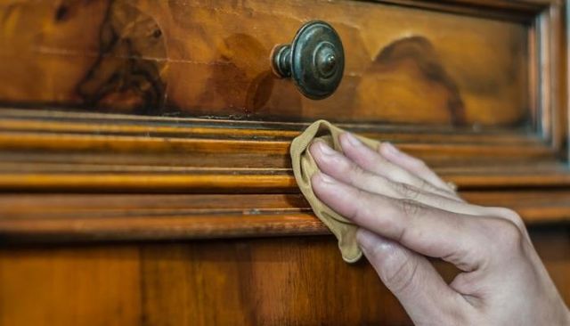 close view of a hand using a beige rag to polish a wooden sideboard