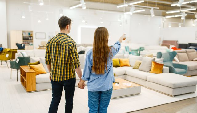 view of a couple holding hands with one of them pointing across a furniture store of sofas