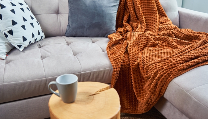 A plush rust colored blanket is thrown on a gray couch with pillows.