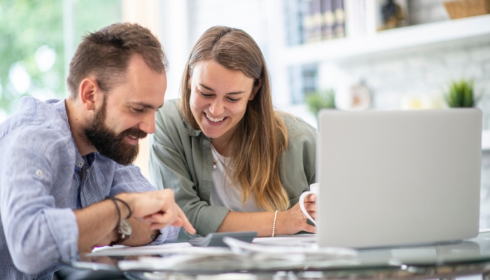 A smiling man and woman sit with a laptop and a calculator