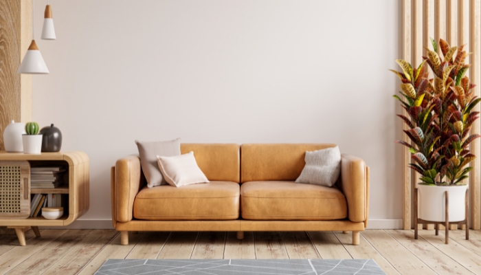 A leather loveseat sits in a neutral color room with a plant and a retro side table.