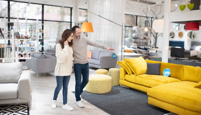 A couple walks through a furniture showroom and points to a yellow couch.