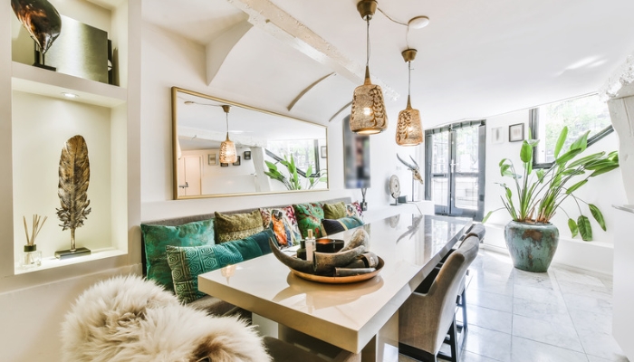A white and green dining room with many boho decorations and pillows. 