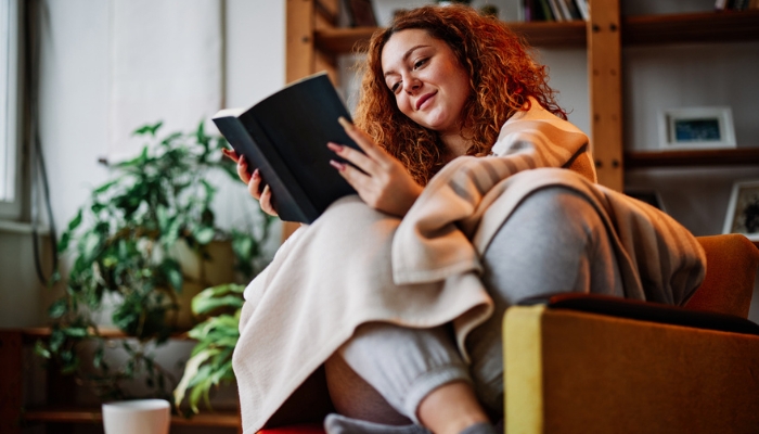 A redheaded woman sits curled up in a chair reading a book.