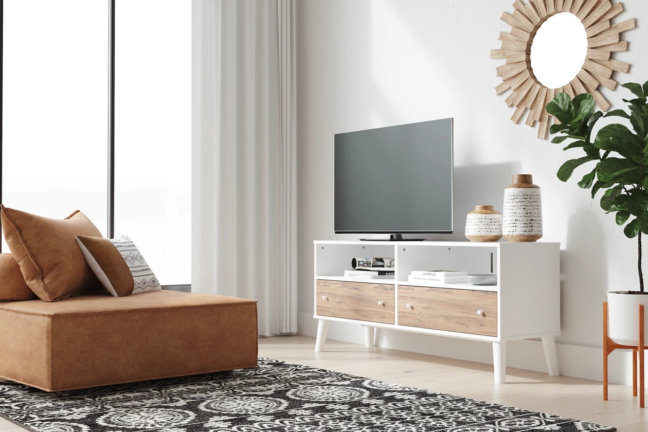 A white modern TV stand sits against a wall in front of a low profile chair