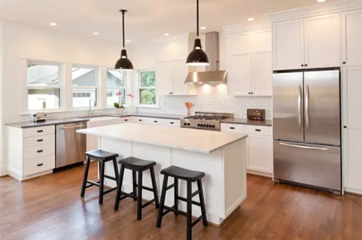 white kitchen with black countertops, an island with black seating, and stainless steel appliances