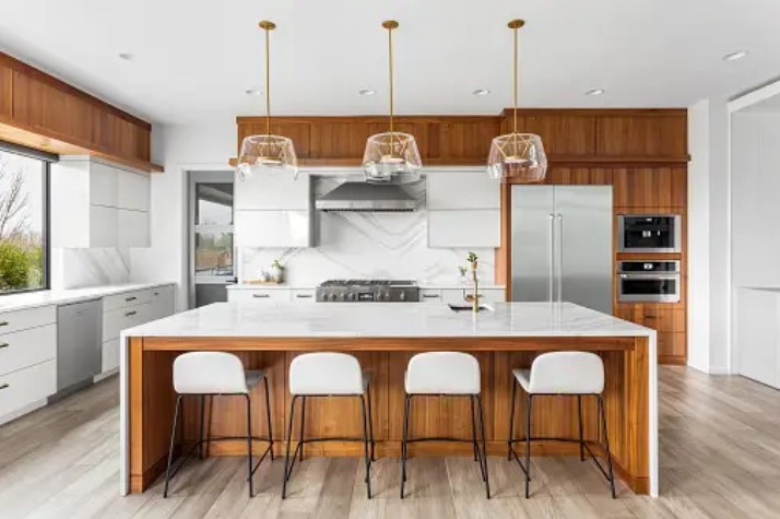 white kitchen with wooden cabinets and a kitchen island with seating, island has a white waterfall countertop and white stools.