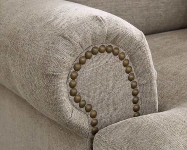 closeup view of a beige upholstered oversized chair arm with nailhead trim