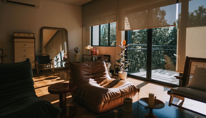 A leather armless chair in front of windows covered with shades, sun shining through