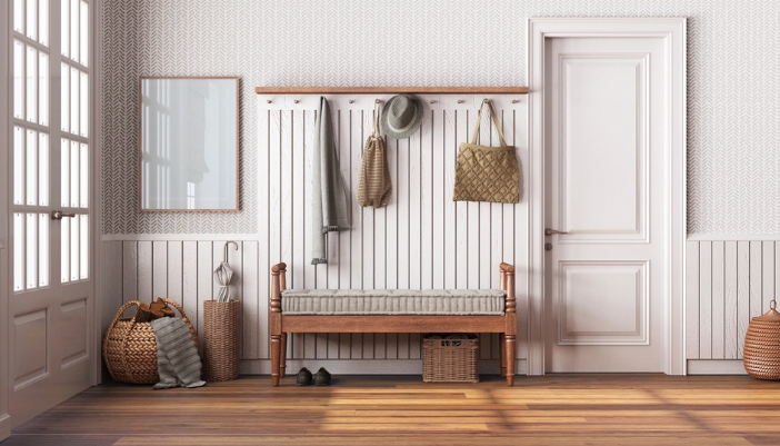 A wooden bench rests in front of a white wooden wall. There are hooks and baskets around the bench.