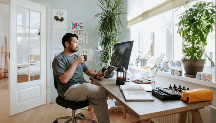 A man drinks coffee in his sweats while sitting in a bright home office.