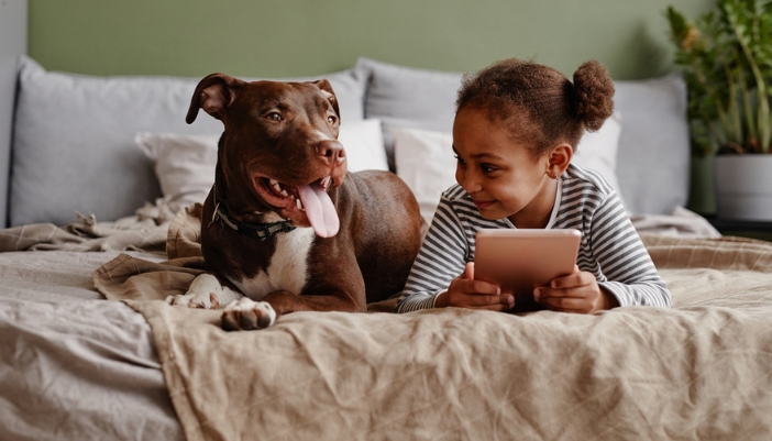 A young girl and a large brown dog lay side-by-side on a couch.