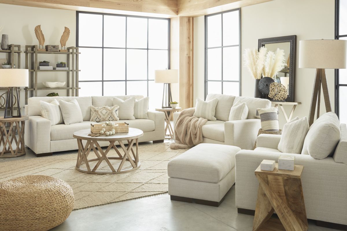 front view of a casual living room with a white oversized chair and ottoman, loveseat, and sofa with beige accents throughout the room.