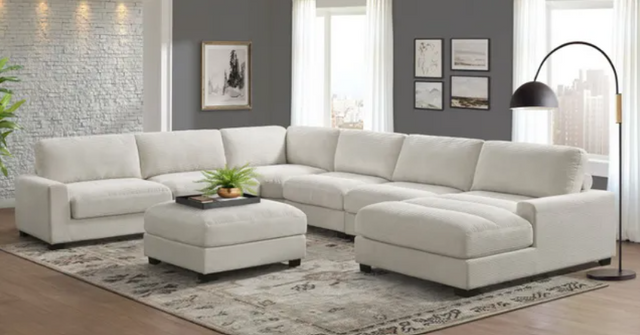 front view of a modern living room with white brick and grey walls, and a white sectional chaise sofa with an ottoman