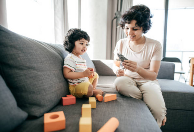 side view of a mother and her toddler playing with blocks and toys on a grey sectional sofa