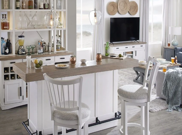 front view of a modern living room with a white home bar and cabinetry, stocked with various glassware and bottles 