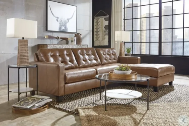 side view of a brown leather chaise sofa in a rustic loft with a large window in the background