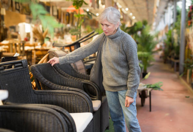 view of a woman walking through an outdoor furniture store and touching a brown wicker chair 