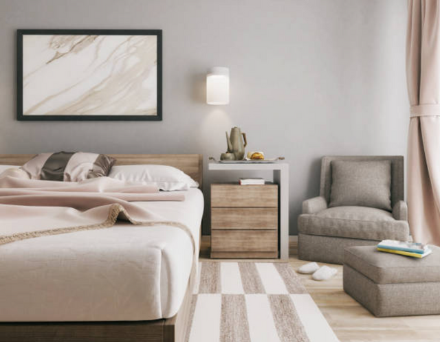 front view of an oversized tall back chair in a bedroom corner with an ottoman and bed