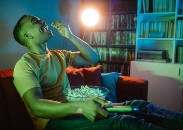 front view of a man smiling while eating popcorn on a large reg oversized chair in his living room