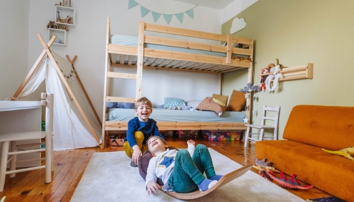 Two brothers play together on a rocking toy in their bedroom/playroom.