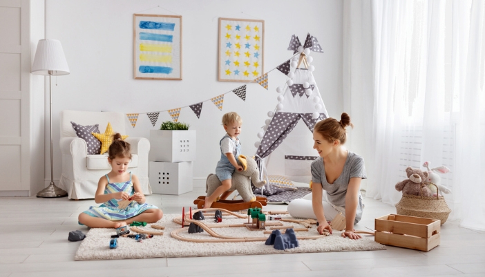 A mother plays with her two small children on the floor of their home playroom.