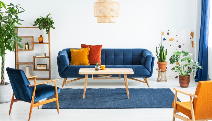 A brightly lit living room with a large blue couch, a blue chair, and an orange chair. 
