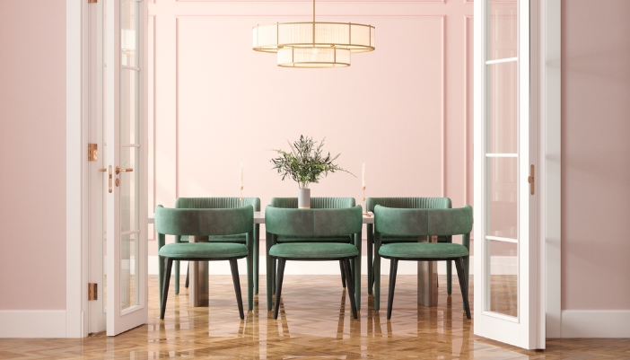 A dining table with green chairs sits in front of a light pink wall.