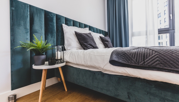 A bed with a blue velvent headboard and frame with white blankets.