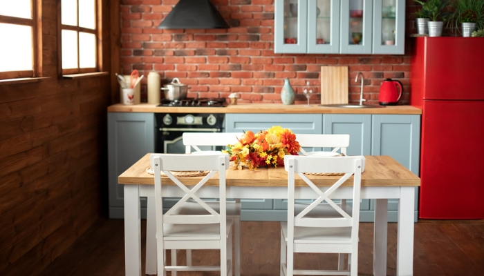 A dining room sits in a kitchen with blue cabinets and retro red appliances.
