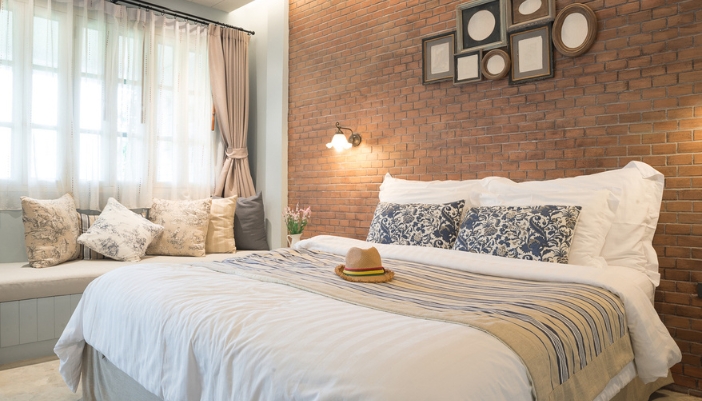 A warm lit bedroom with white bedsheets and many throw pillows.