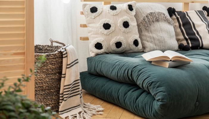 An oversized blue cushion sits on the floor with an open book and many textured pillows.